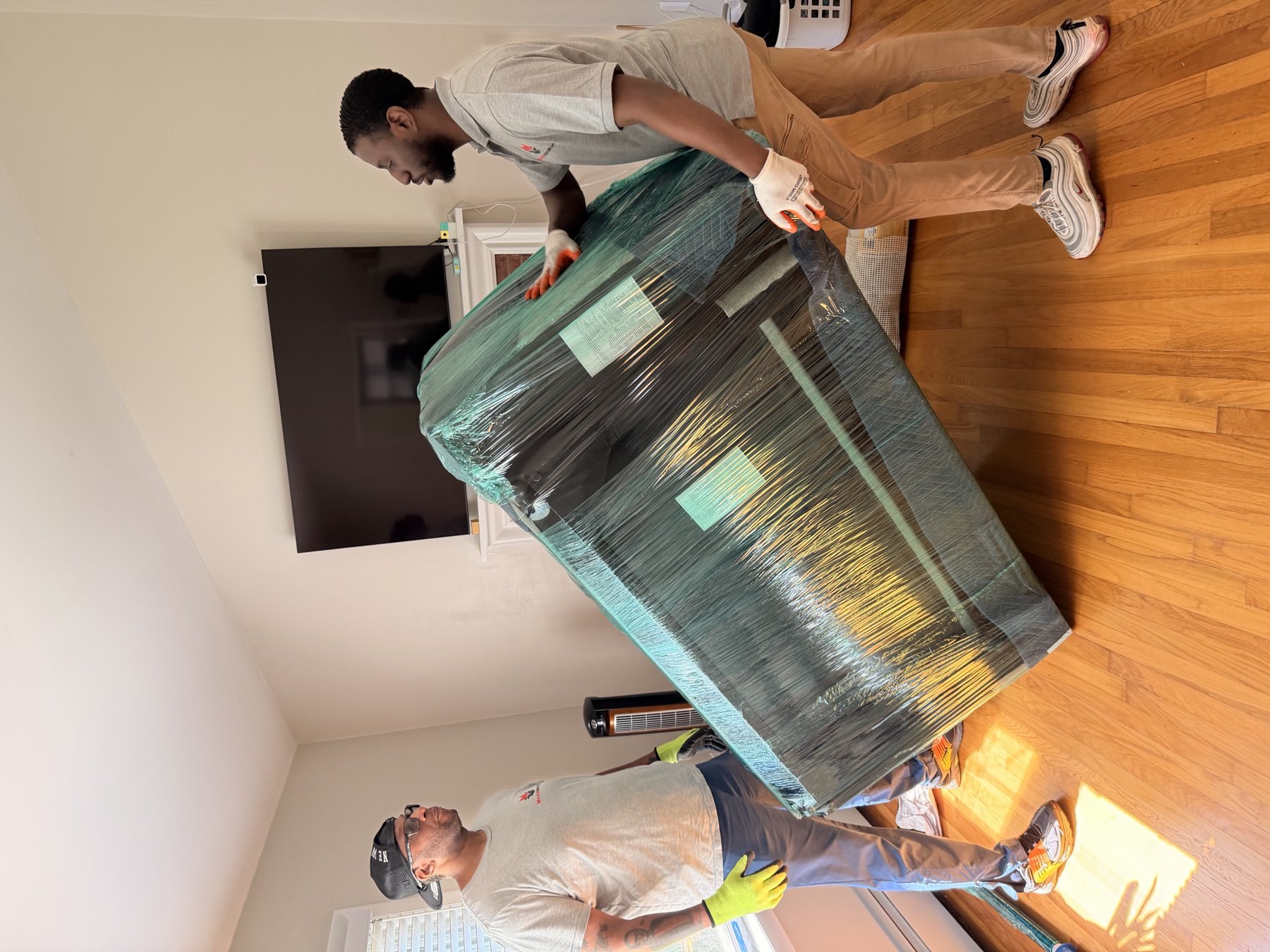Major Movers crew carrying a shrink-wrapped sofa through a living room