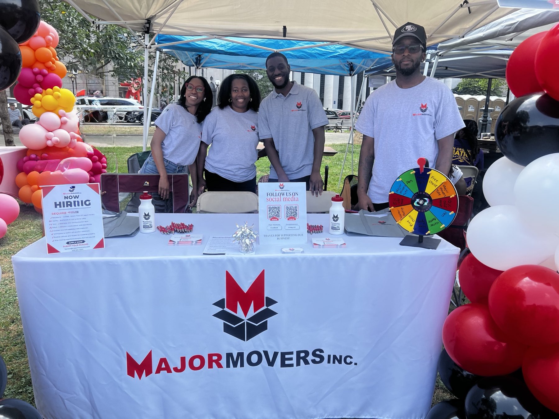 The Major Movers team at a community event behind a branded Major Movers table