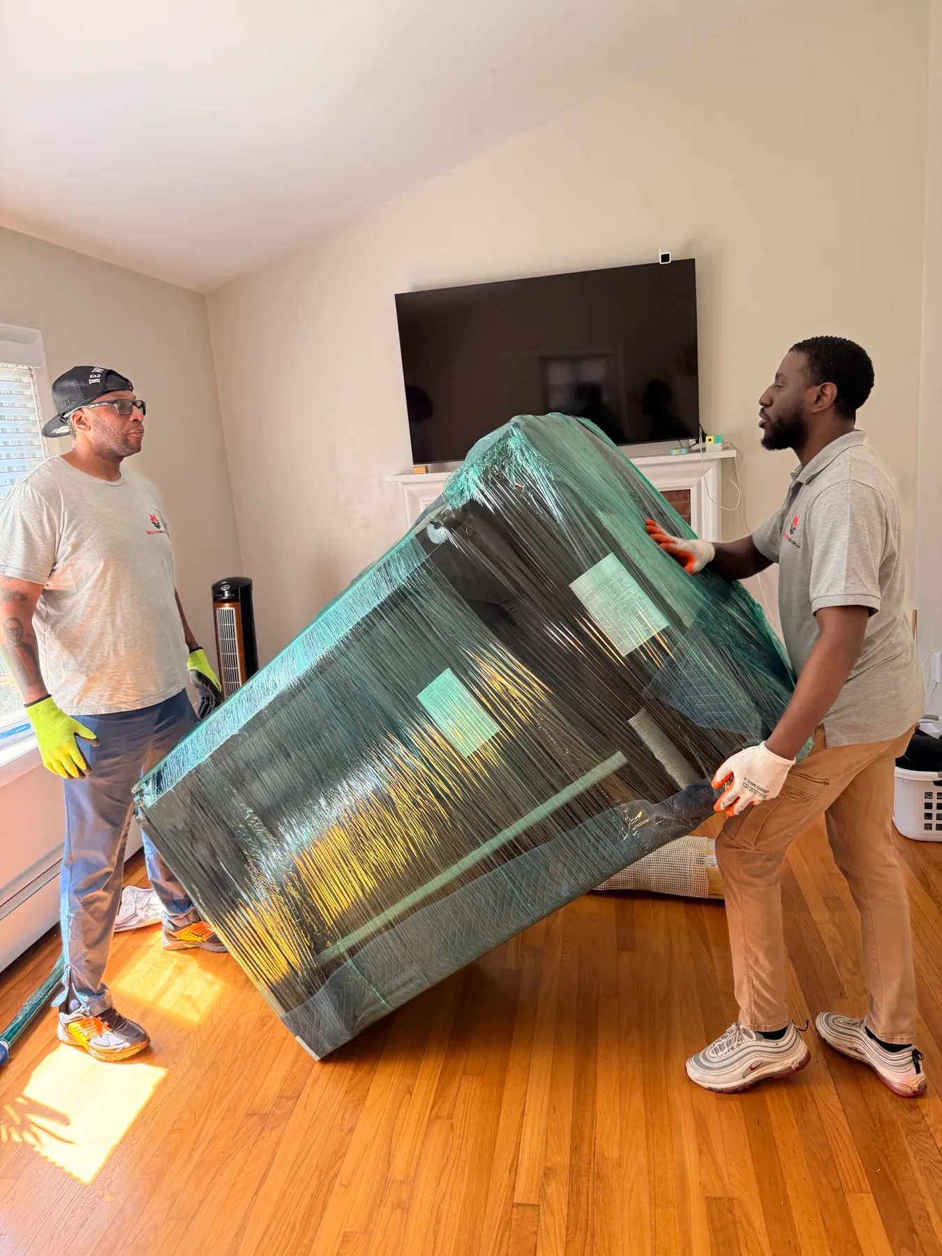 Major Movers crew carrying a shrink-wrapped sofa through a living room